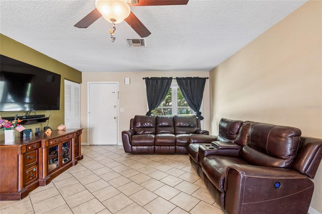 A living room features brown leather sofas, a wooden media console, and tiled flooring — 9473 BAYSIDE COURT, SPRING HILL, FL