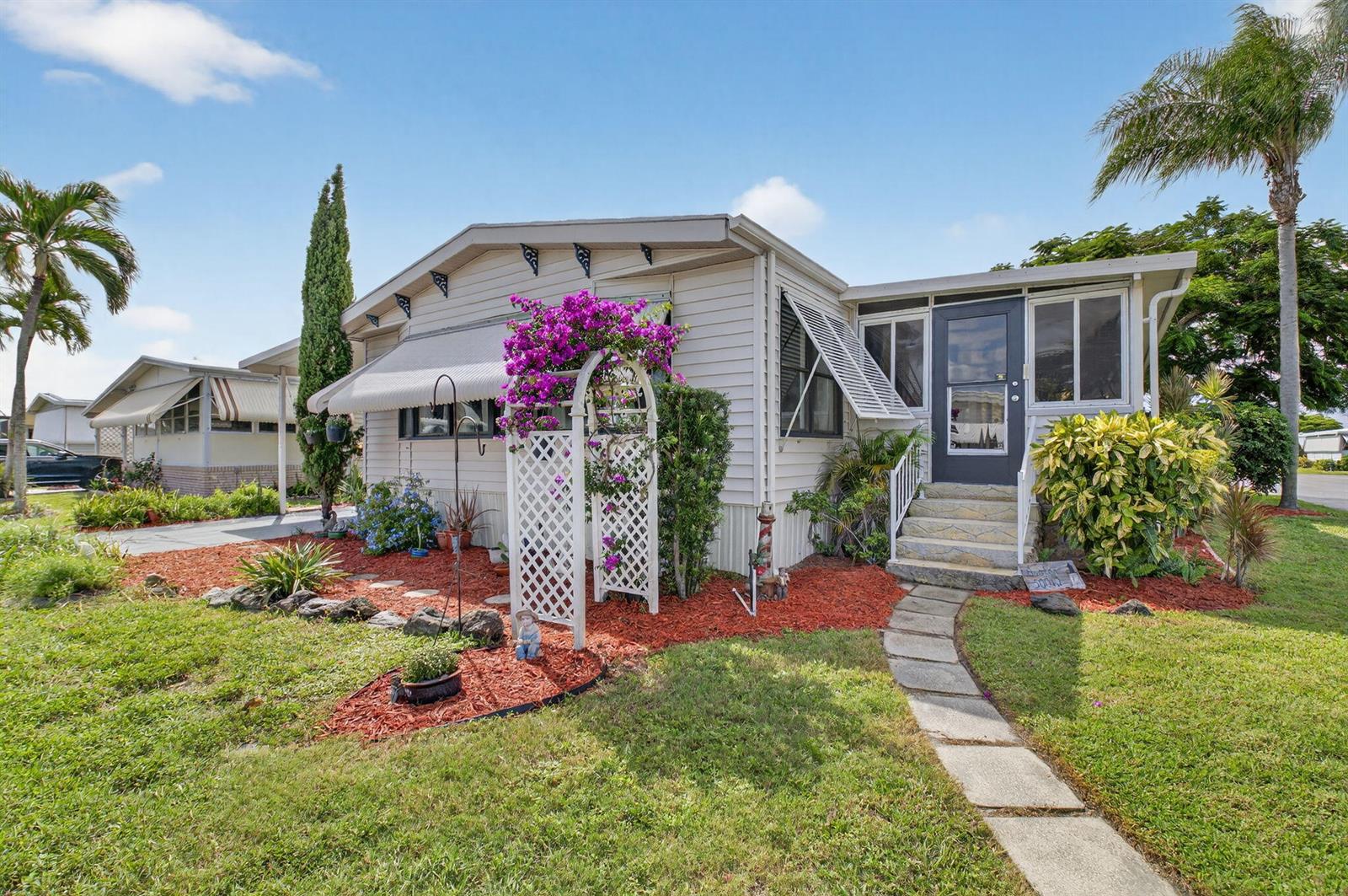 A single-story mobile home with a white trellis, red mulch, and a stone walkway — 50012 Hacha, Boynton Beach FL 33436, BOYNTON BEACH, FL