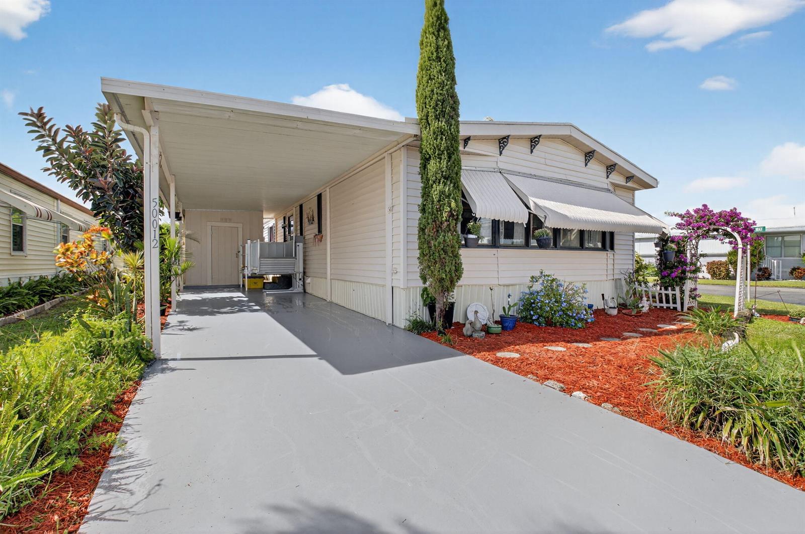 A single-story mobile home with a carport, light siding, and a red mulch front yard — 50012 Hacha, Boynton Beach FL 33436, BOYNTON BEACH, FL