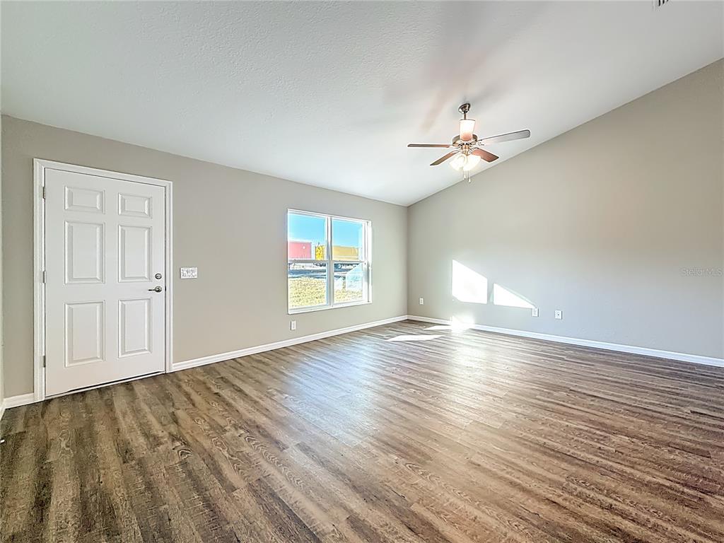 An empty living room features wood-look flooring, a vaulted ceiling with a fan, and a window — 14805 SW 32ND PLACE, OCALA, FL