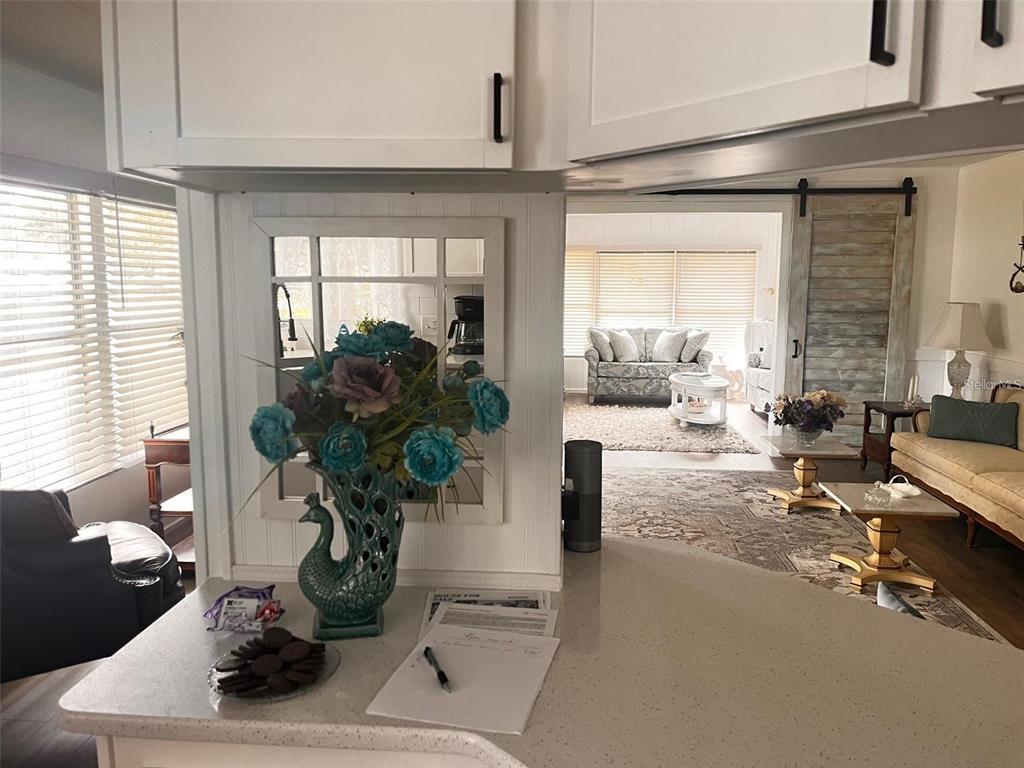 A kitchen counter with a peacock vase overlooks a living room with a sliding barn door — 33 BOBCAT TRAIL, WILDWOOD, FL