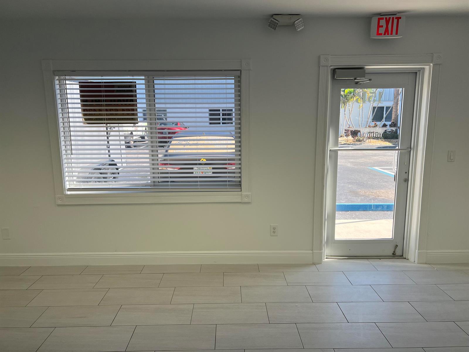 A bright room with light tile flooring, a window with blinds, and an exit door — 1312 Commerce Lane # 15b, Jupiter FL 33458, JUPITER, FL