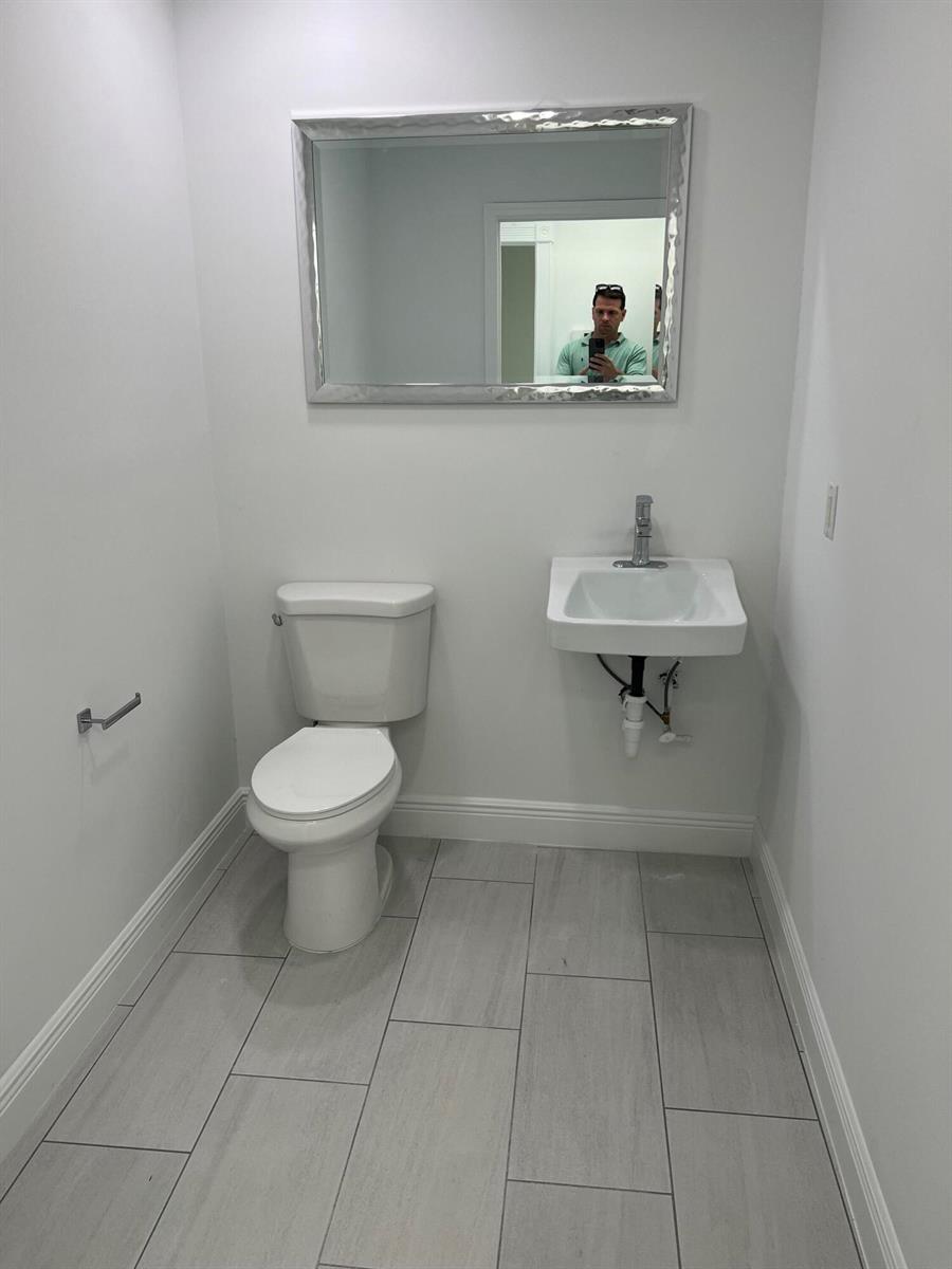 A small half bathroom features a white toilet, wall-mounted sink, and gray tile flooring — 1312 Commerce Lane # 15b, Jupiter FL 33458, JUPITER, FL
