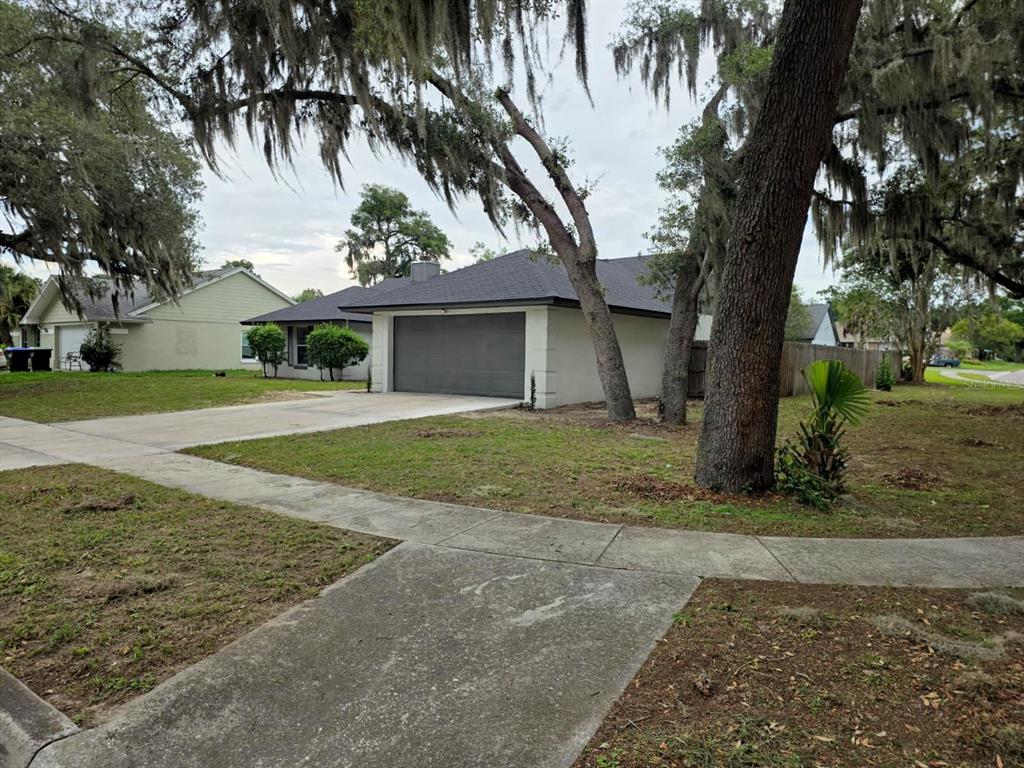 A single-story house with a gray garage door and large trees in the front yard — 6476 PREAKNESS DRIVE, ORLANDO, FL