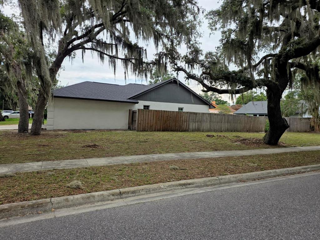 A side view of a single-story house with a wooden fence and large oak trees — 6476 PREAKNESS DRIVE, ORLANDO, FL