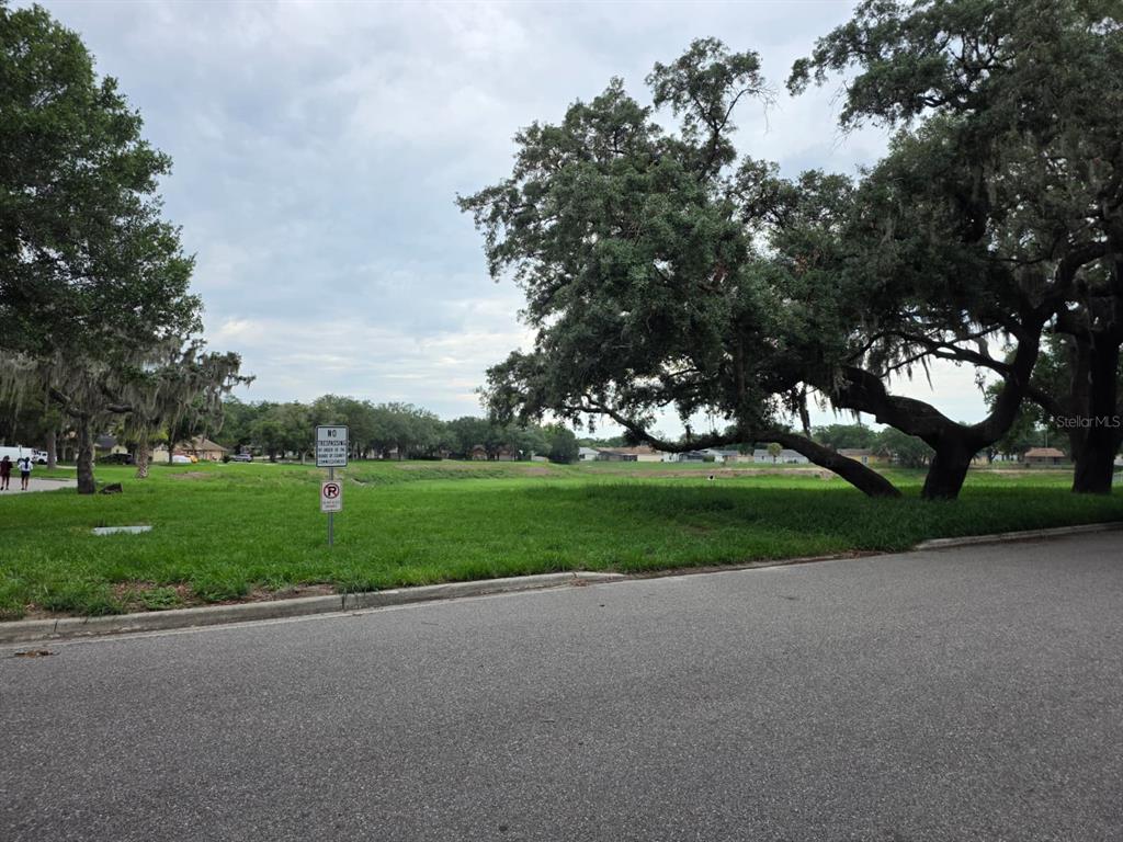 A grassy vacant lot with large oak trees sits next to a paved residential street — 6476 PREAKNESS DRIVE, ORLANDO, FL