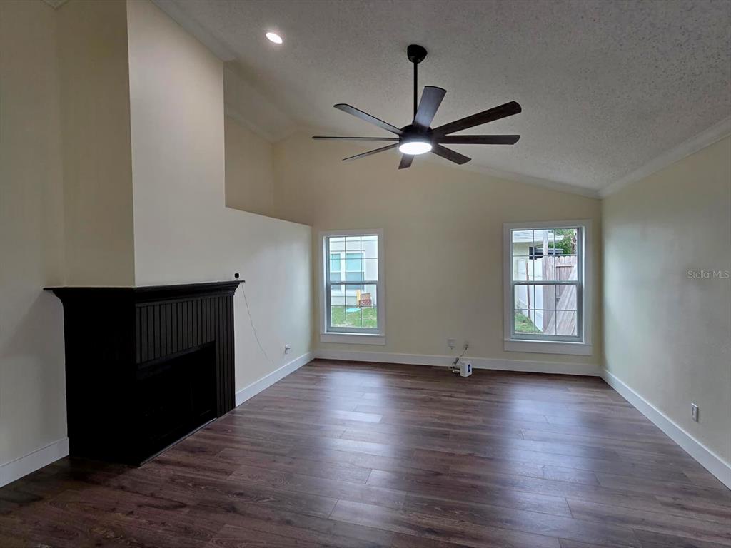 A living room features a black fireplace, vaulted ceiling, ceiling fan, and wood-look flooring — 6476 PREAKNESS DRIVE, ORLANDO, FL