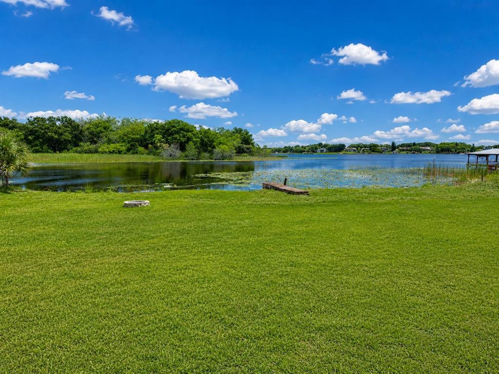 A grassy backyard leads to a lake with a small wooden dock and lily pads — 13619 LAKE BOULEVARD, WINTER GARDEN, FL