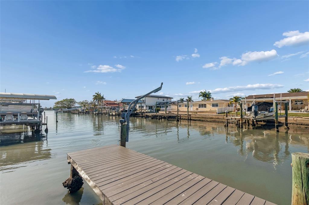A wooden dock extends into a canal lined with houses, boat lifts, and palm trees — 4415 CLEARWATER HARBOR DRIVE N, LARGO, FL