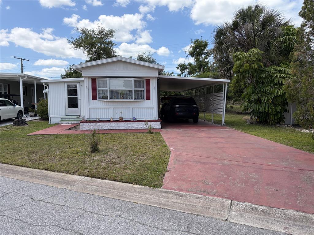 A single-story mobile home features a white exterior, a front bay window, and a carport — 4833 BOCA RATON AVENUE, SARASOTA, FL