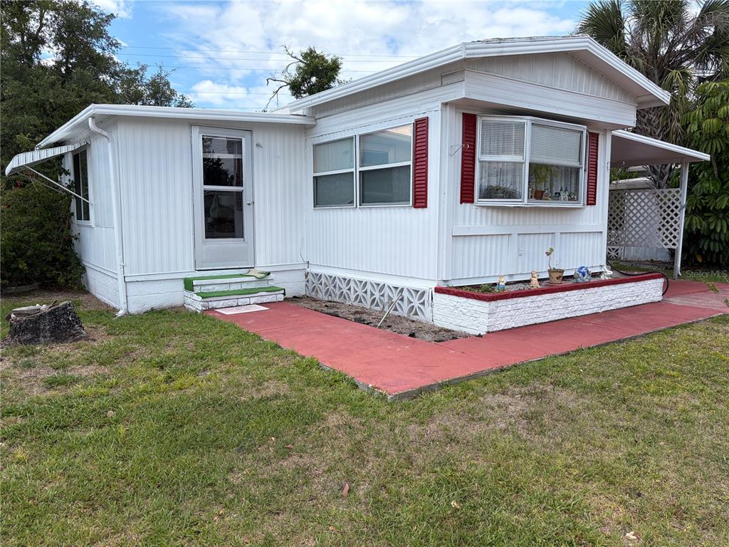 A white mobile home with red shutters and a red concrete walkway in the yard — 4833 BOCA RATON AVENUE, SARASOTA, FL