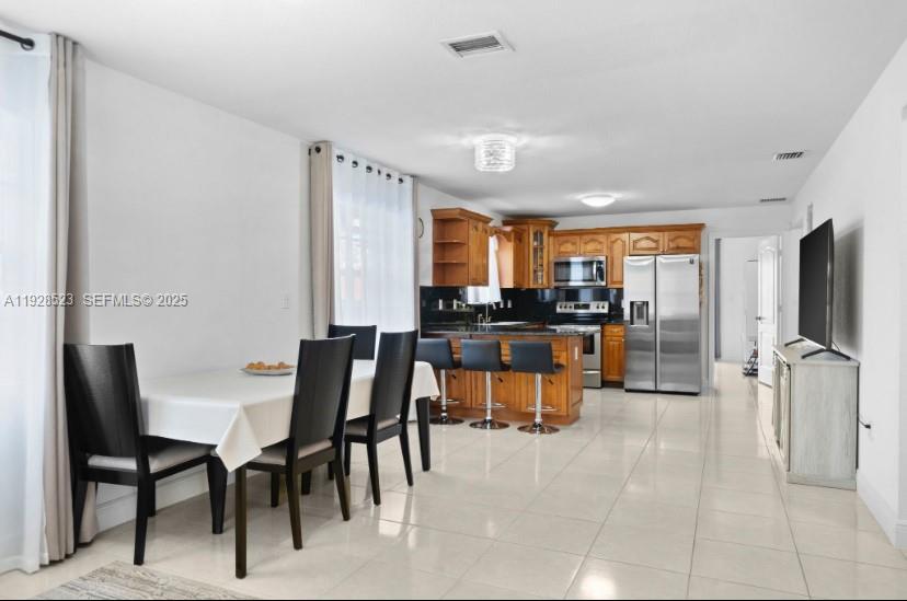 A dining area and kitchen feature light tile floors, wooden cabinetry, and stainless steel appliances — 701 NE 6th St, Hallandale Beach FL 33009, HALLANDALE BEACH, FL