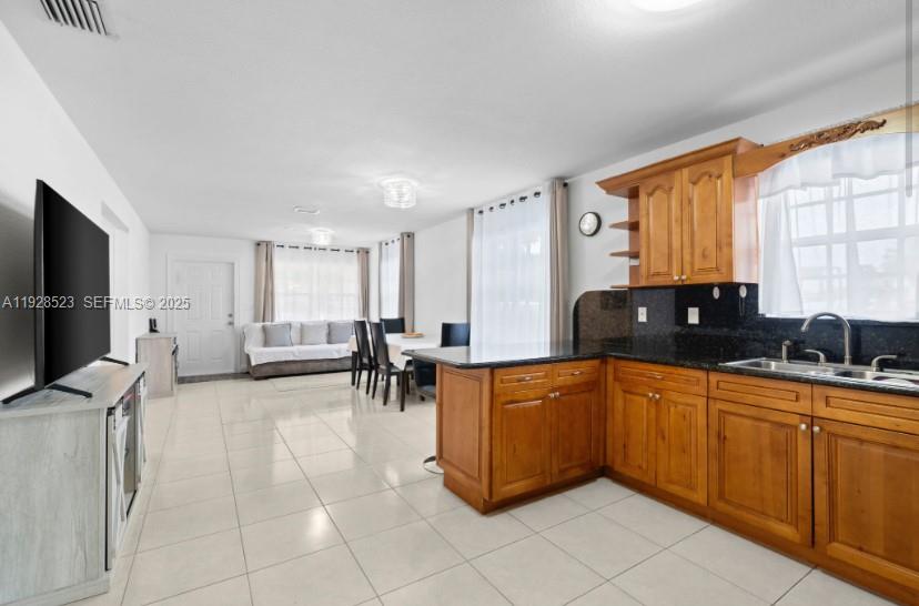 A kitchen with wood cabinets and a granite countertop opens into a dining and living area — 701 NE 6th St, Hallandale Beach FL 33009, HALLANDALE BEACH, FL