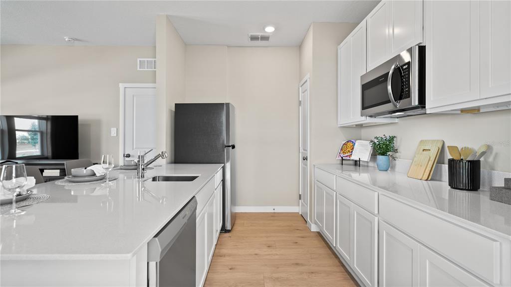 A kitchen features white cabinets, quartz countertops, stainless steel appliances, and light wood-look flooring — 2242 JENNIO DRIVE, HAINES CITY, FL