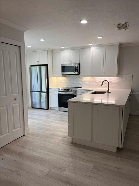 A modern kitchen features white cabinetry, stainless steel appliances, and a central island with seating — 4044 CORKWOOD COURT, PALM HARBOR, FL