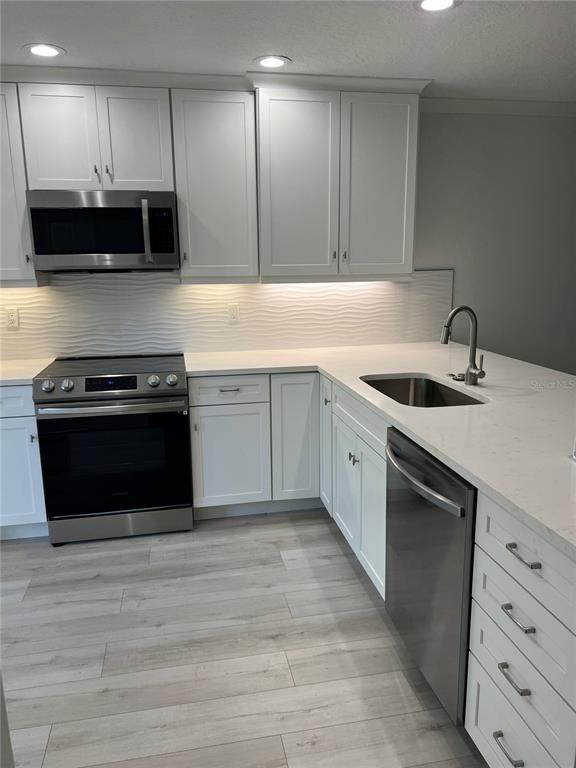 A modern kitchen features white cabinets, stainless steel appliances, and light-colored wood-look flooring — 4044 CORKWOOD COURT, PALM HARBOR, FL