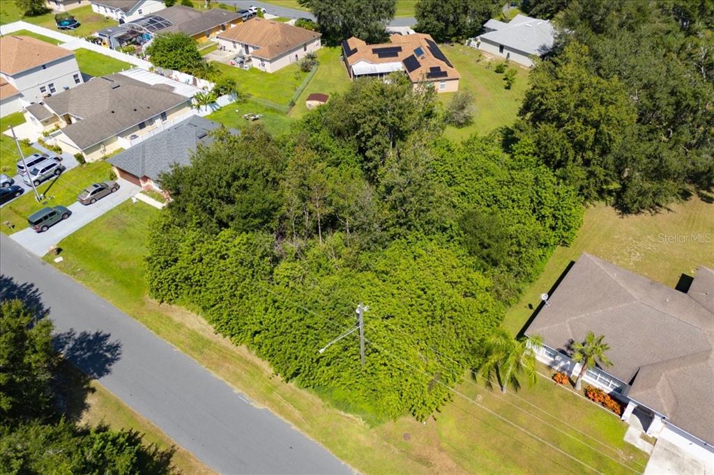An aerial view shows a vacant, tree-covered residential lot situated between several suburban houses — 0 CANNES DRIVE, KISSIMMEE, FL