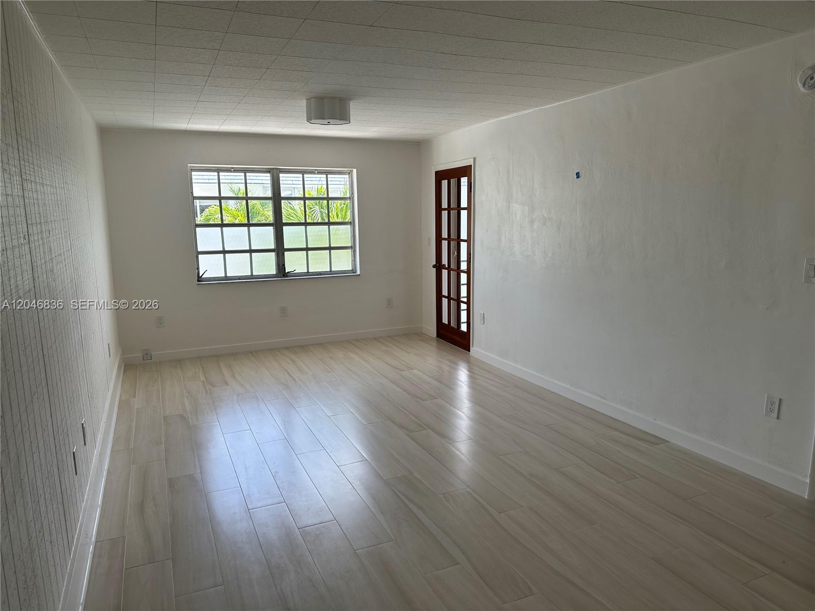 An empty room features light wood-look flooring, white walls, a grid window, and a glass-paneled door — 251 Galen Dr # 302, Key Biscayne FL 33149, KEY BISCAYNE, FL