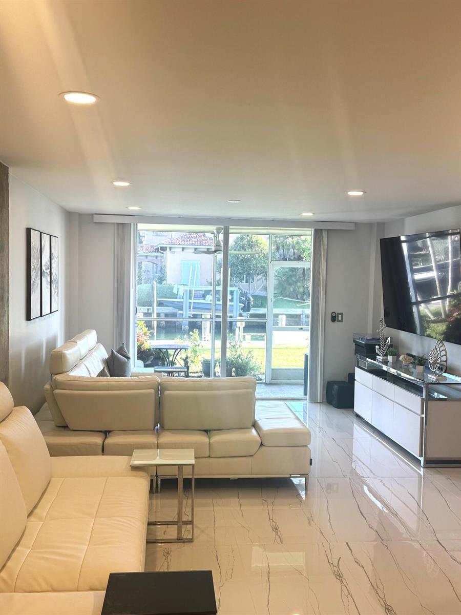 A living room with white leather sofas, marble-look tile floors, and a view of water — 105 Paradise Harbour Boulevard # 108, North Palm Beach FL 33408, NORTH PALM BEACH, FL