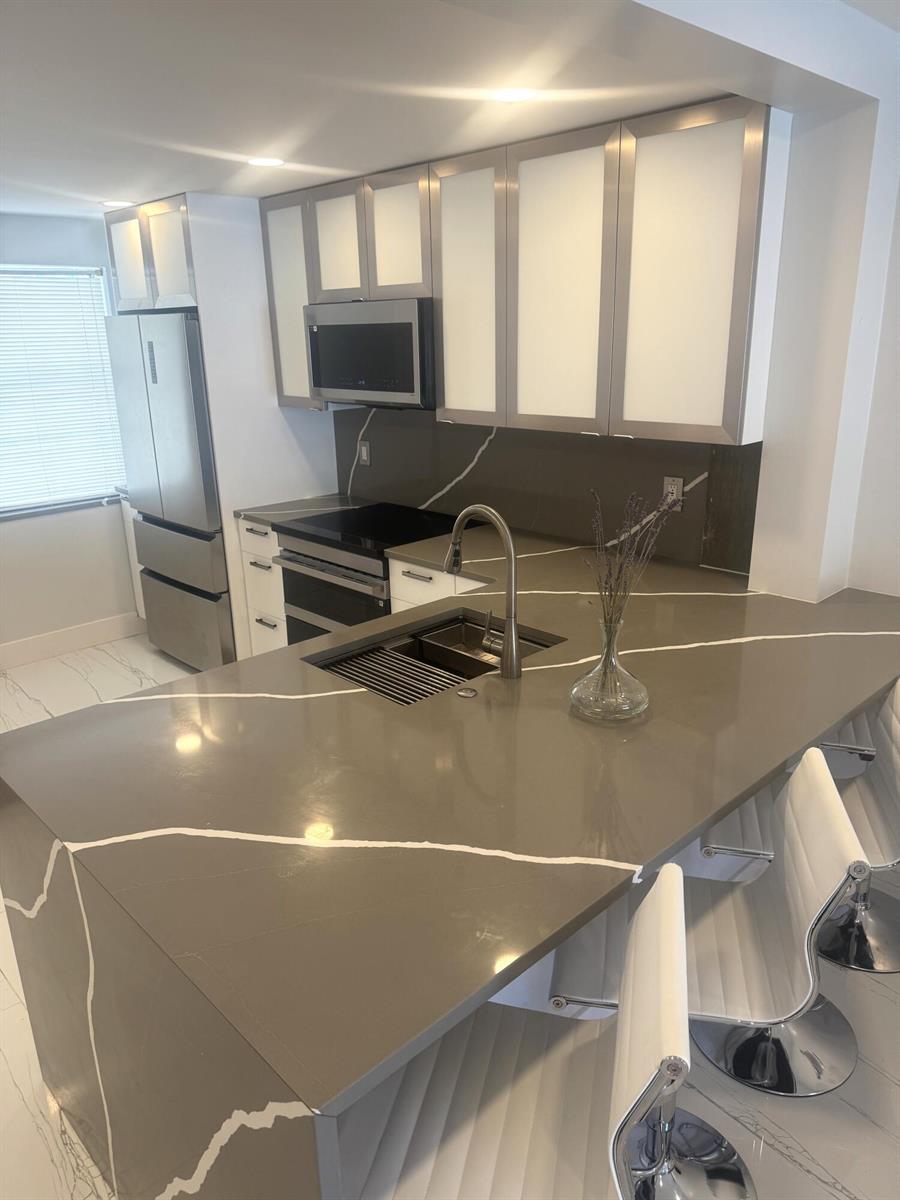 A modern kitchen features gray quartz countertops with white veining, stainless steel appliances, and cabinetry — 105 Paradise Harbour Boulevard # 108, North Palm Beach FL 33408, NORTH PALM BEACH, FL