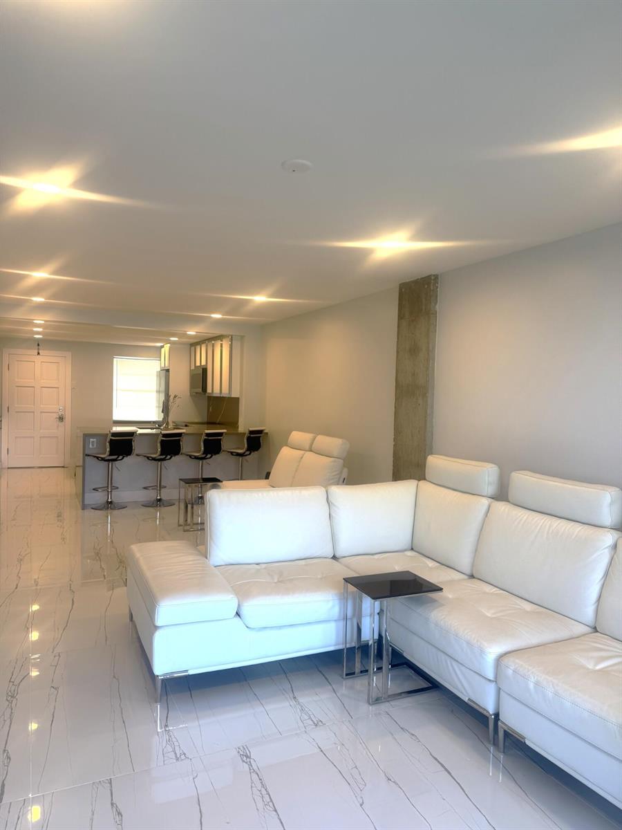 A living room with white leather sofas, marble-look tile floors, and an open kitchen area — 105 Paradise Harbour Boulevard # 108, North Palm Beach FL 33408, NORTH PALM BEACH, FL