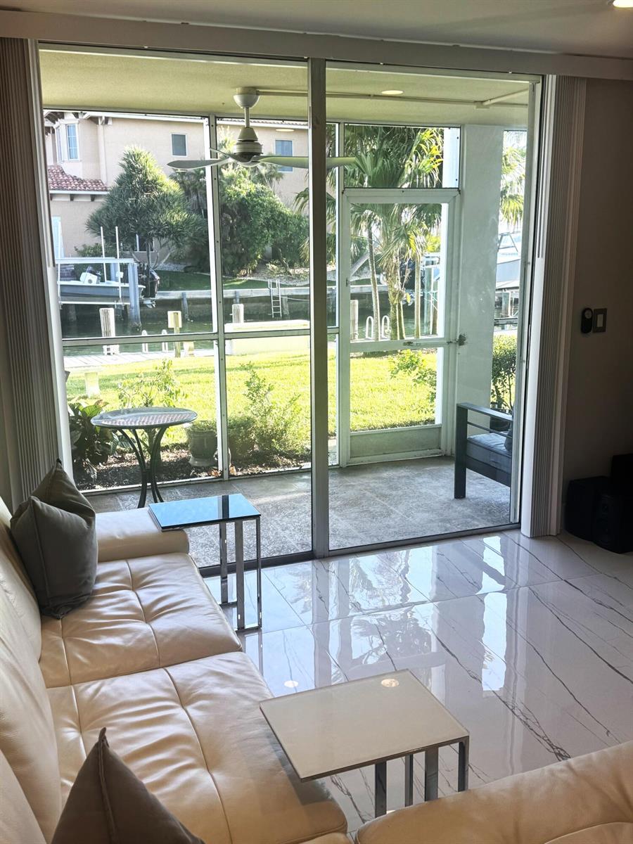 A living room with white tile floors and a sofa overlooking a screened patio and canal — 105 Paradise Harbour Boulevard # 108, North Palm Beach FL 33408, NORTH PALM BEACH, FL