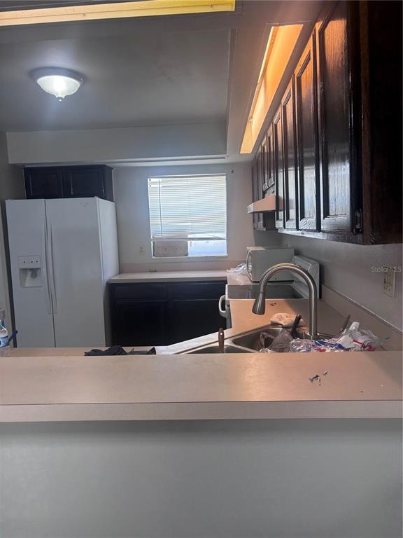 A kitchen features dark wood cabinets, a white refrigerator, and a stainless steel sink — 624 JAGUAR COURT, POINCIANA, FL