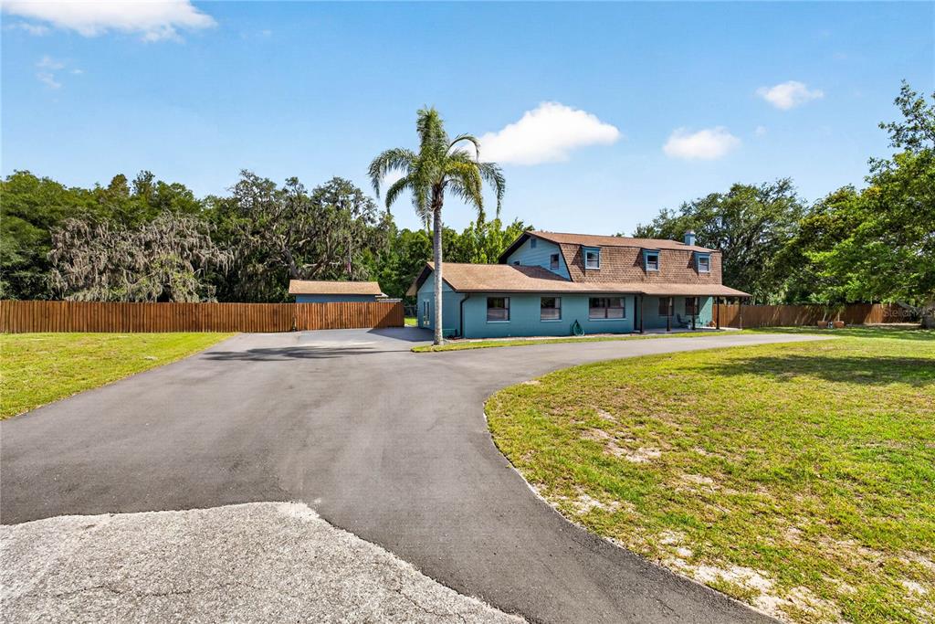 A two-story teal house with a brown roof sits behind a large paved driveway — 9400 SAVOY COURT, NEW PORT RICHEY, FL