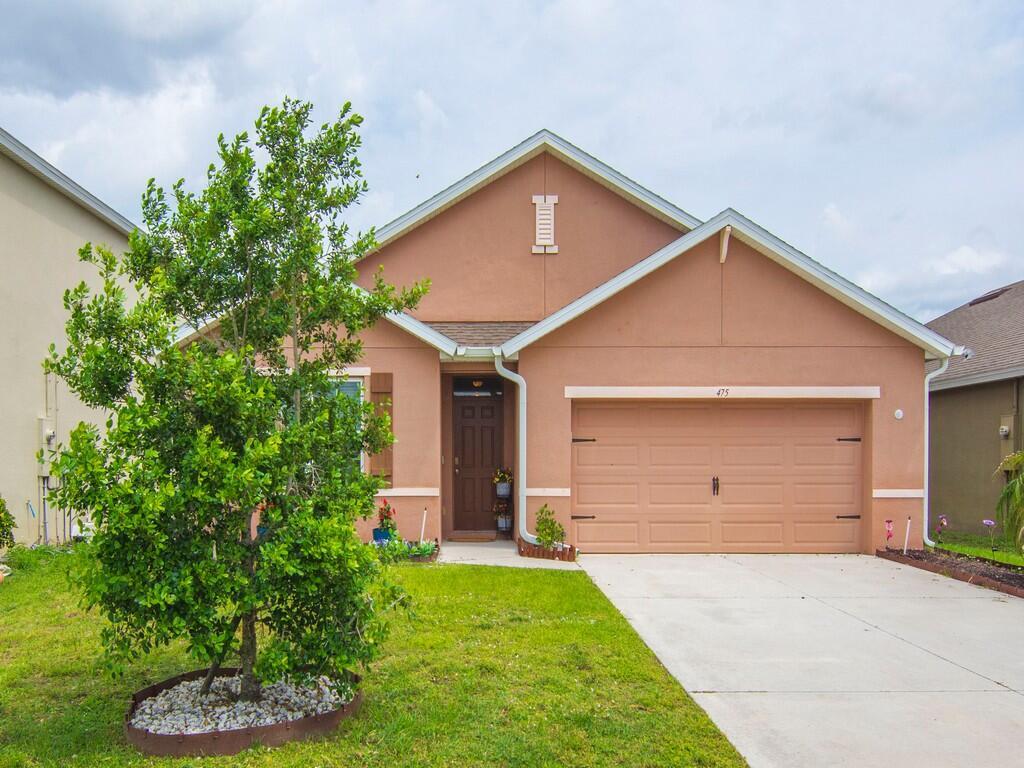 A single-story house with a tan stucco exterior, a two-car garage, and a front lawn — 475 SW Moray Dr Drive, Palm Bay FL 32908, PALM BAY, FL