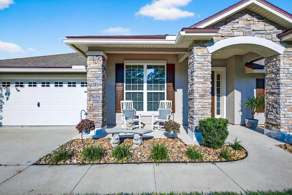 A stone-accented house exterior features a front porch with two rocking chairs and a bench — 86434 MOONLIT WALK CIRCLE, YULEE, FL