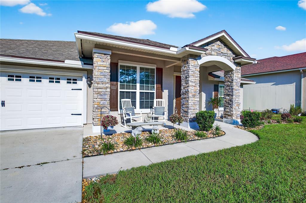 A single-story house exterior features a stone-accented entryway, a two-car garage, and a front porch — 86434 MOONLIT WALK CIRCLE, YULEE, FL
