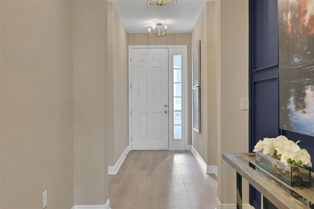 A bright entryway features light wood flooring, beige walls, a white front door, and blue accents — 17320 WILD DAISY DRIVE, WINTER GARDEN, FL