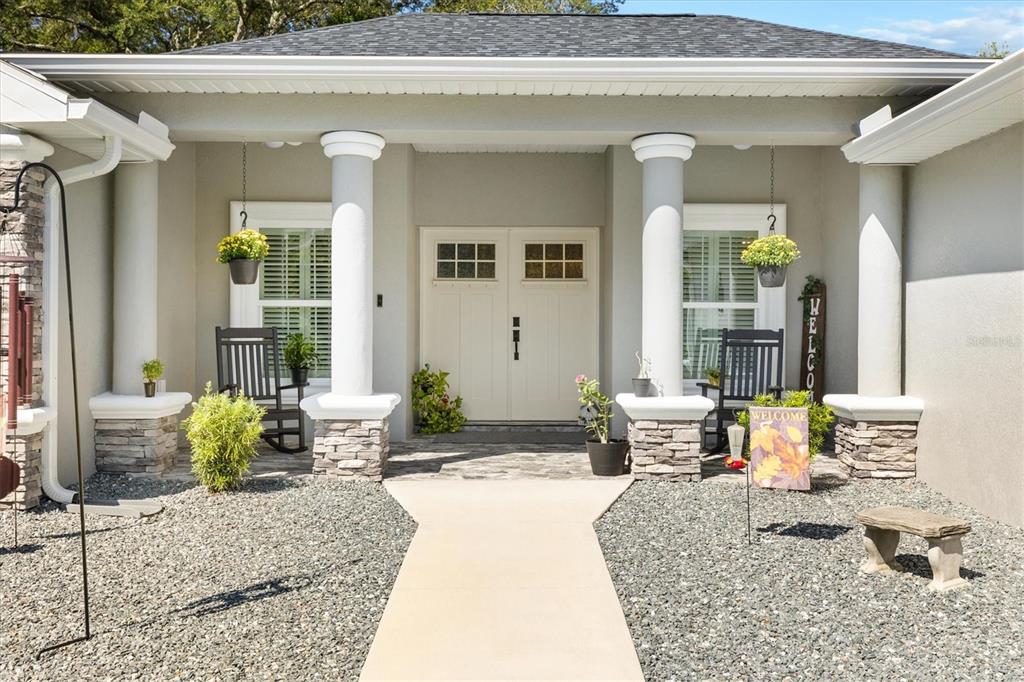 A front porch with stone columns, rocking chairs, and a double door entrance — 16394 SE 89TH TERRACE, SUMMERFIELD, FL
