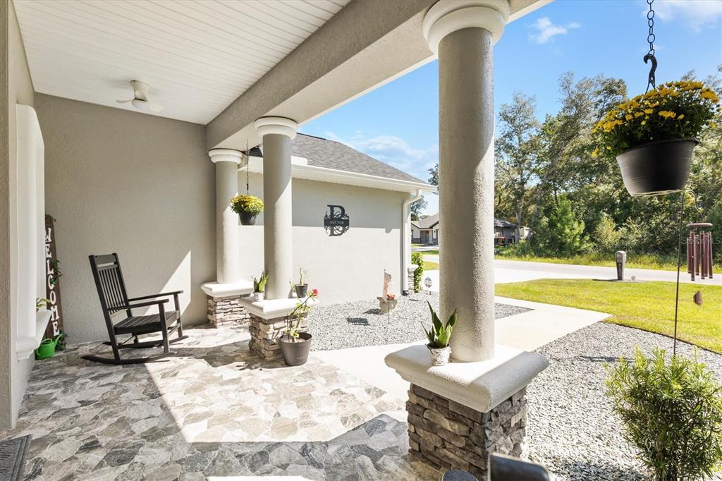 A covered front porch features stone flooring, columns with stone bases, and a rocking chair — 16394 SE 89TH TERRACE, SUMMERFIELD, FL