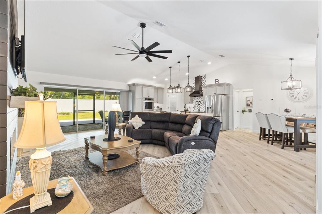 An open-concept living room and kitchen featuring light wood flooring and a large sectional sofa — 16394 SE 89TH TERRACE, SUMMERFIELD, FL