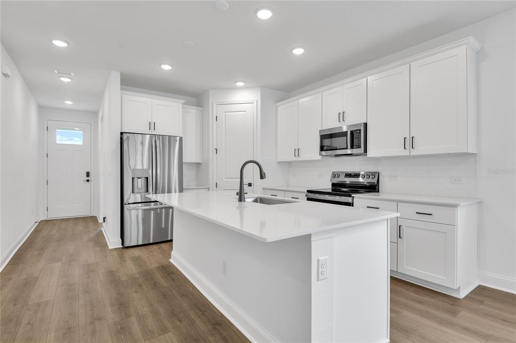 A modern kitchen features white cabinetry, a central island with a sink, and stainless appliances — 198 ENCLAVE AVENUE, PALM COAST, FL
