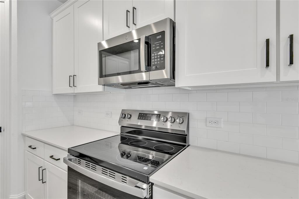 A kitchen features white cabinets, a stainless steel microwave and stove, and a subway tile backsplash — 198 ENCLAVE AVENUE, PALM COAST, FL