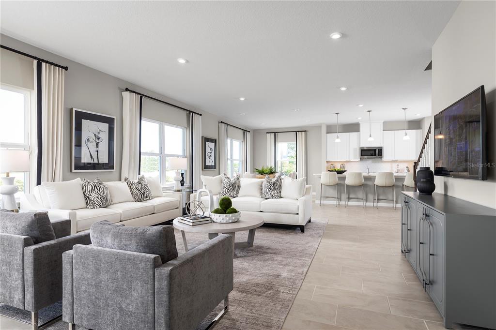 A bright, open-concept living room and kitchen featuring white sofas, gray armchairs, and tile flooring — 7348 SW 107TH LANE, OCALA, FL