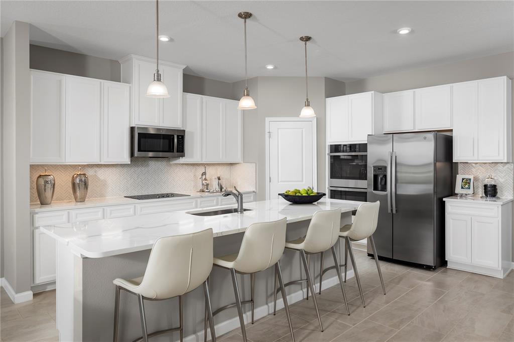 A modern kitchen features white cabinets, a large quartz island, and stainless steel appliances — 7348 SW 107TH LANE, OCALA, FL