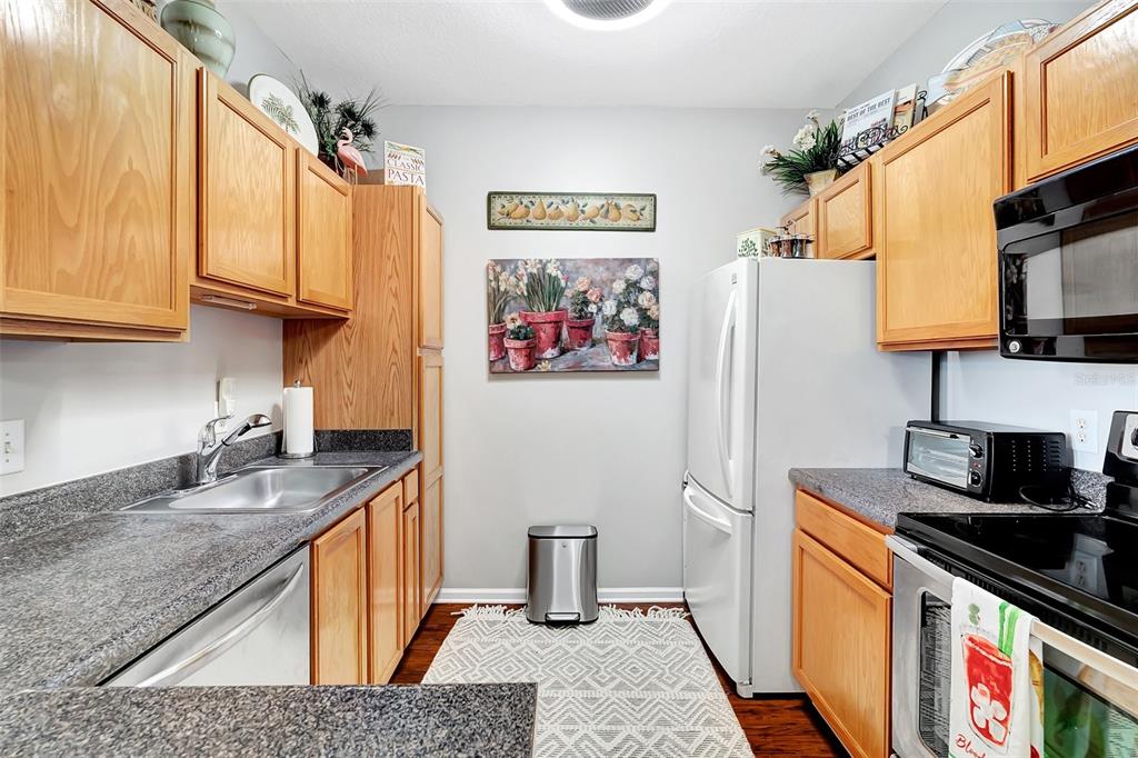 A galley kitchen features light wood cabinets, granite countertops, stainless steel appliances, and a rug — 4802 51ST STREET W UNIT 412, BRADENTON, FL