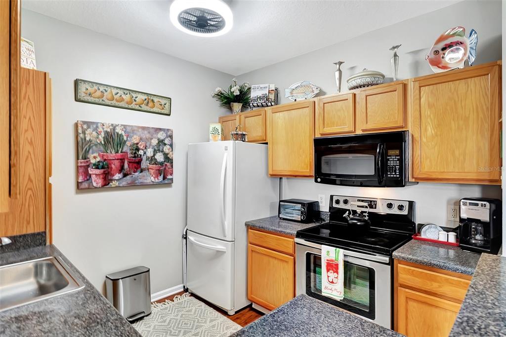 A kitchen features wood cabinets, a white refrigerator, a black stove, and a microwave — 4802 51ST STREET W UNIT 412, BRADENTON, FL
