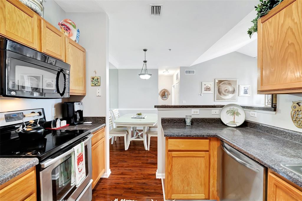 A kitchen with wood cabinets, dark countertops, and stainless steel appliances overlooks a dining area — 4802 51ST STREET W UNIT 412, BRADENTON, FL