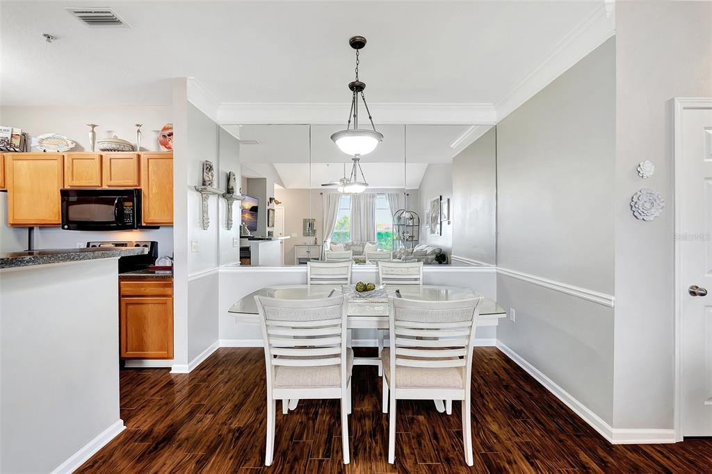 A dining area features a glass-top table, white chairs, wood flooring, and a mirrored wall — 4802 51ST STREET W UNIT 412, BRADENTON, FL