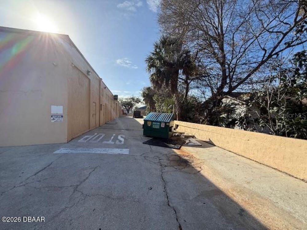 A paved alleyway runs between a tan building wall and a low retaining wall — 1396 N NOVA ROAD, DAYTONA BEACH, FL
