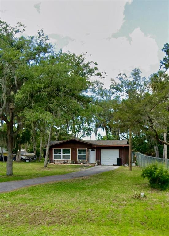 A single-story house with a brown exterior, attached garage, and a driveway surrounded by trees — 10661 W HALLS RIVER ROAD, HOMOSASSA, FL