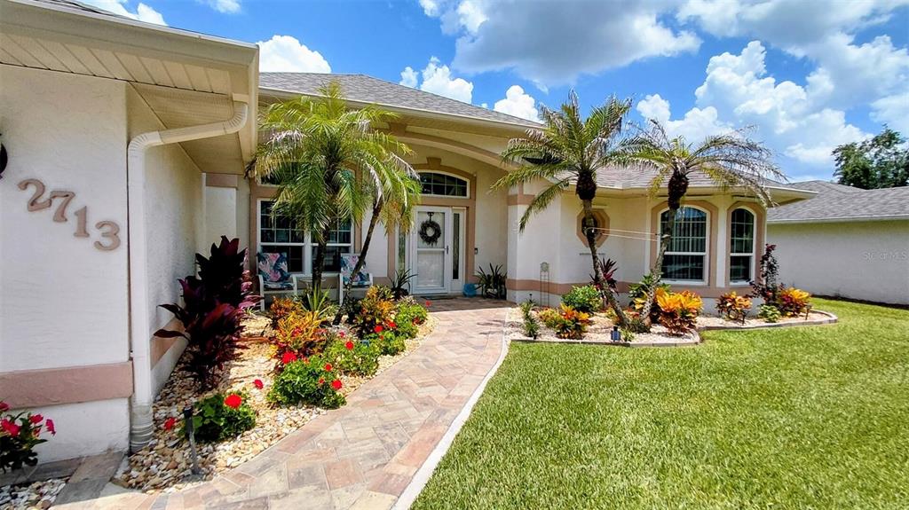 The exterior of a single-story house features a paved walkway, palm trees, and landscaping — 2713 TURNBULL ESTATES DRIVE, NEW SMYRNA BEACH, FL