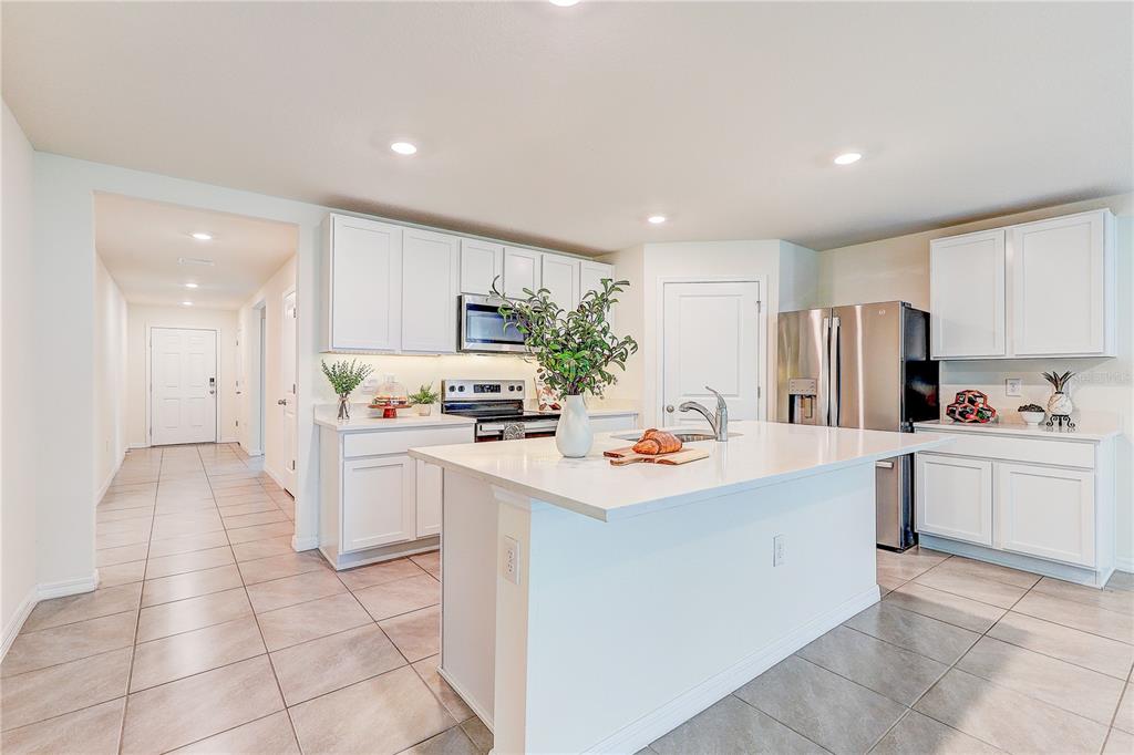 A modern kitchen features white cabinets, stainless steel appliances, a central island, and tiled floors — 13419 CHIPPENDALE STREET, SPRING HILL, FL