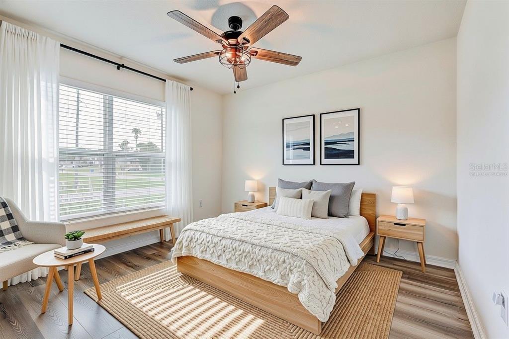 A bedroom with a wooden bed frame, ceiling fan, and large window with white curtains — 13419 CHIPPENDALE STREET, SPRING HILL, FL