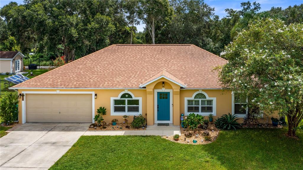 A yellow single-story house with a brown shingled roof, a blue front door, and garage — 1101 MYRTLE LAKE VIEW DRIVE, FRUITLAND PARK, FL
