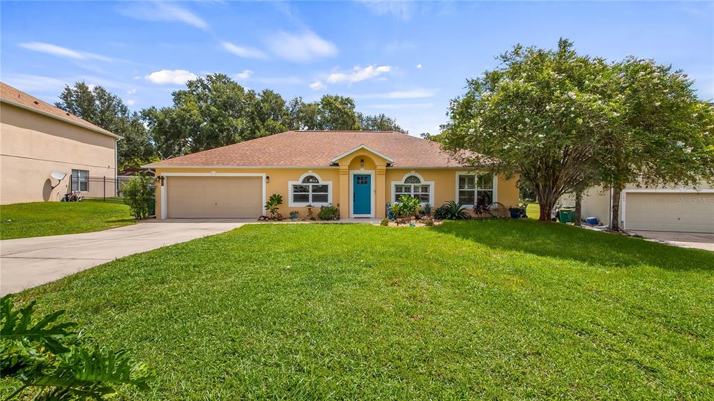A single-story yellow house with a two-car garage and a front lawn under a blue sky — 1101 MYRTLE LAKE VIEW DRIVE, FRUITLAND PARK, FL